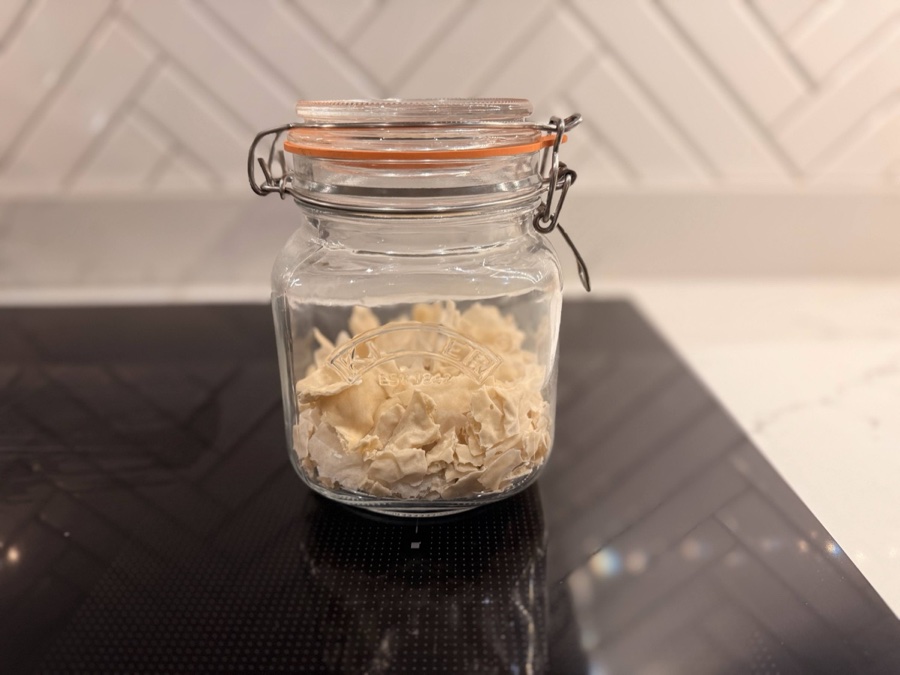 Dried sourdough starter flakes in a Kilner jar on a dark countertop