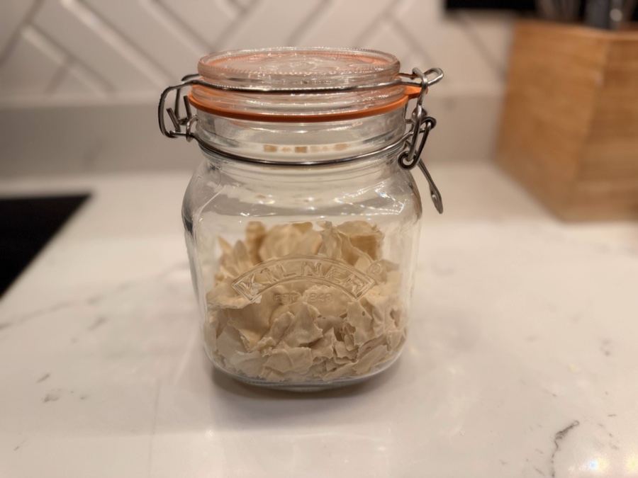 Dried sourdough starter flakes stored in a Kilner jar on a marble countertop