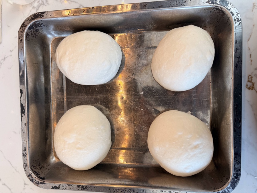 Four smooth sourdough pizza dough balls sitting in a metal baking tray, ready for their second cold rest