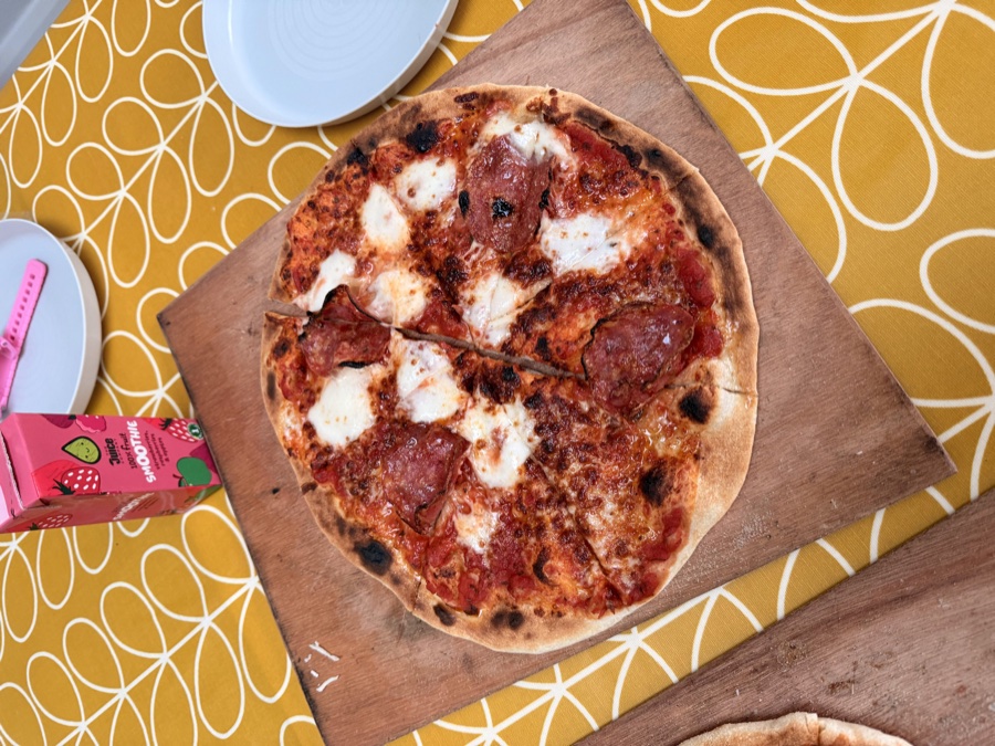 A sourdough pizza with tomato, salami and fresh mozzarella on a wooden board, char spots on the crust
