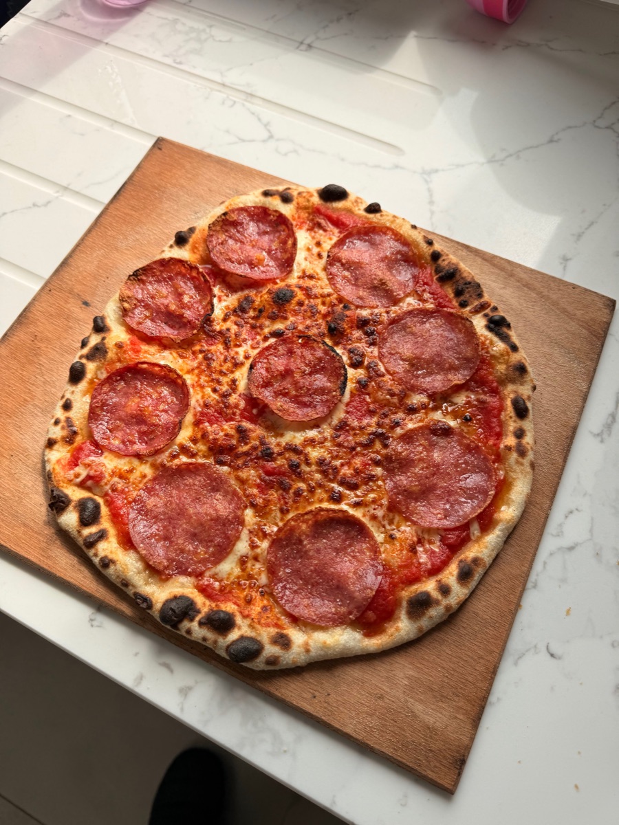 A sourdough pizza with salami and tomato sauce on a wooden peel, deep golden crust with char spots