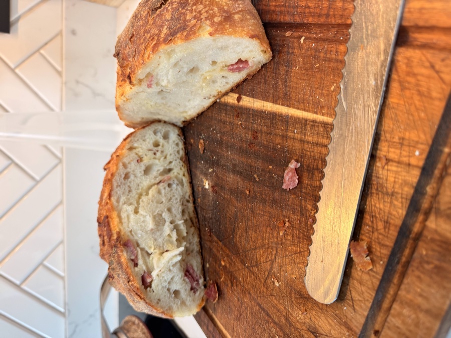Salami and cheese sourdough cut in half showing the open crumb with chunks of salami distributed throughout