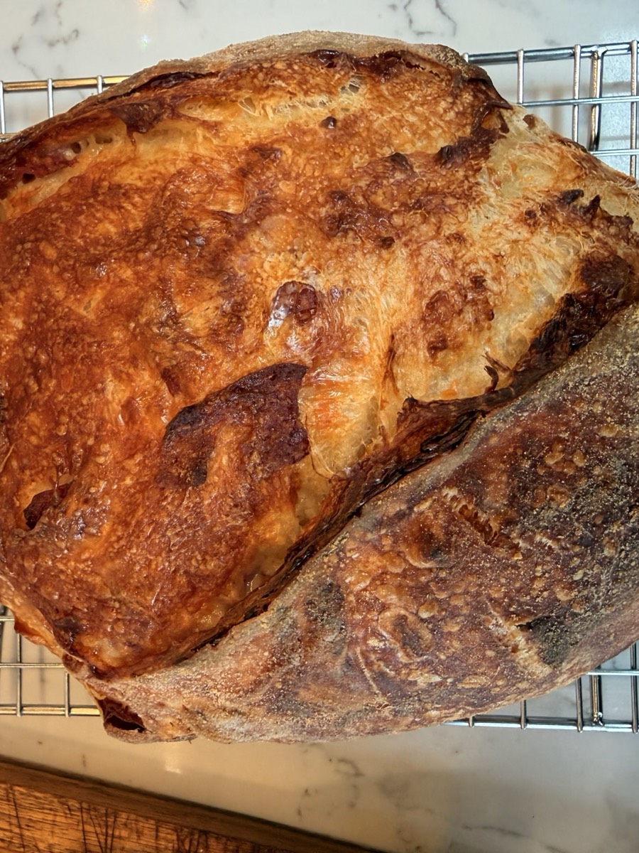 A salami and cheese sourdough boule cooling on a wire rack, with a blistered golden crust and visible crispy salami spots