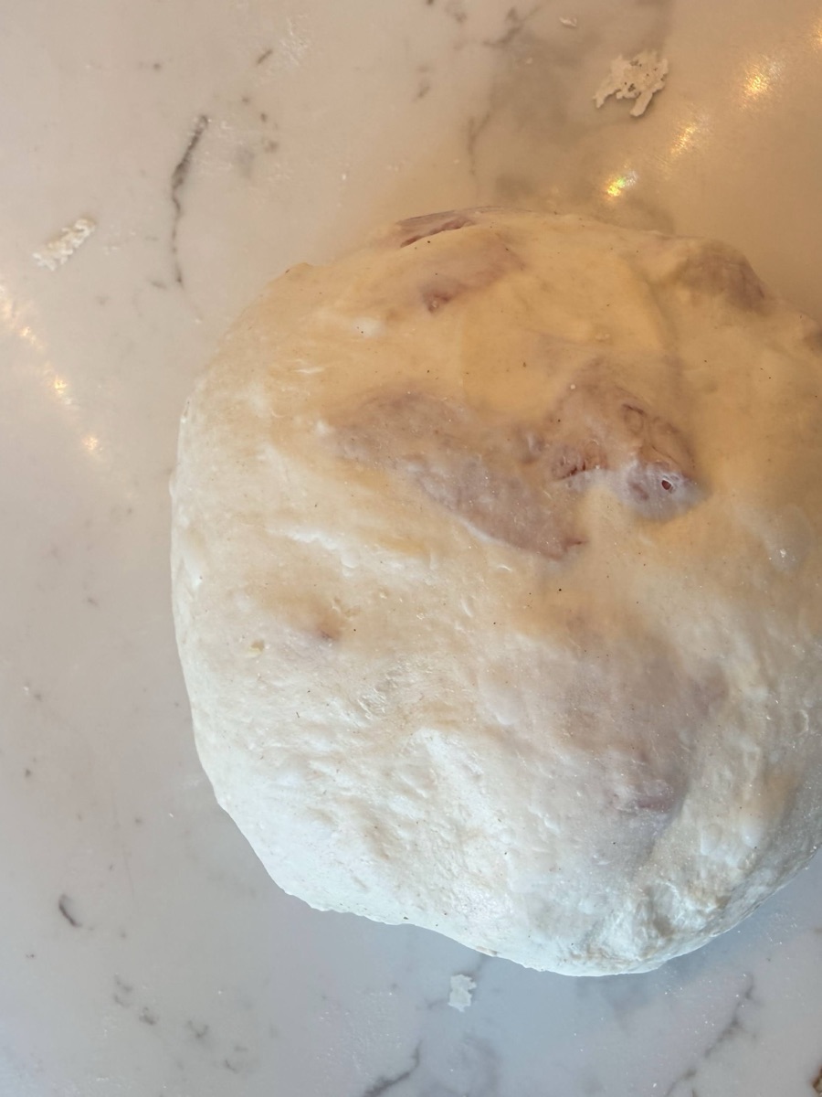 Shaped sourdough boule on the work surface with pieces of salami visible through the dough surface